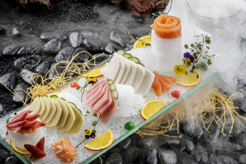 刺身拼摆放在干冰缭绕的黑色鹅卵石上