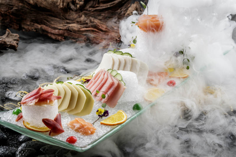 刺身拼摆放在干冰缭绕的黑色鹅卵石上