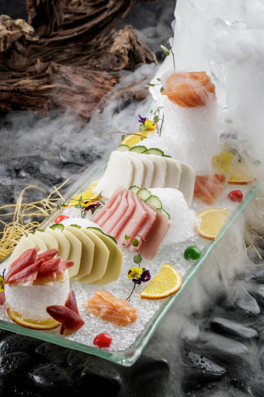 刺身拼摆放在干冰缭绕的黑色鹅卵石上