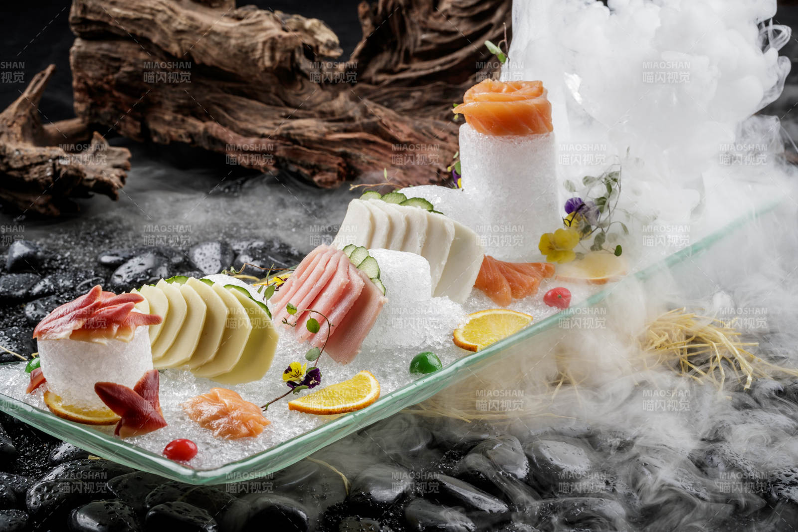 刺身拼摆放在干冰缭绕的黑色鹅卵石上