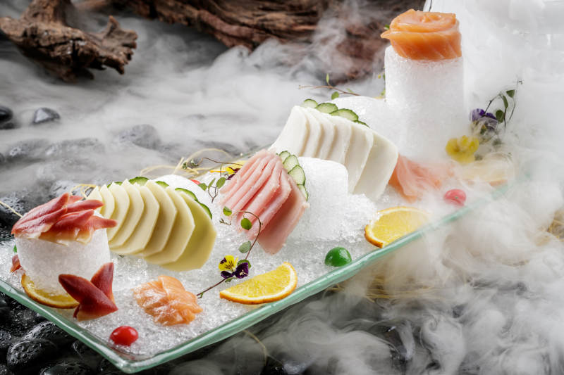 刺身拼摆放在干冰缭绕的黑色鹅卵石上