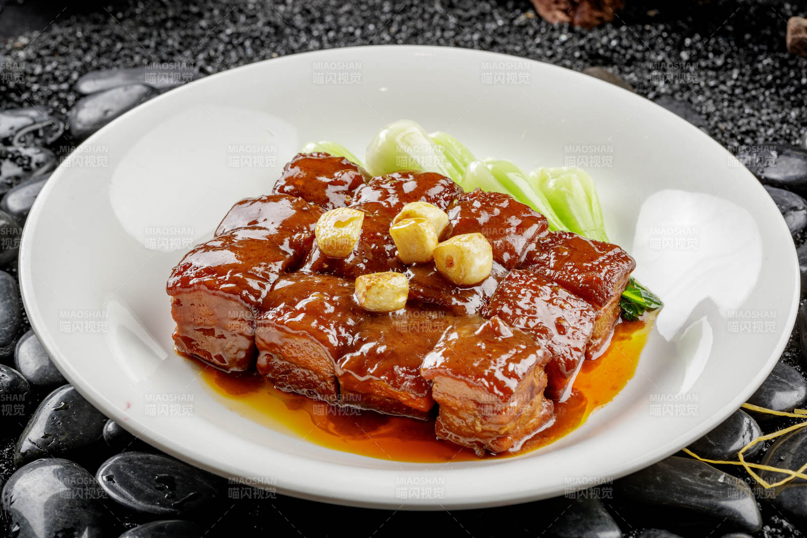 白色圆盘装的毛氏红烧肉摆放在黑色鹅卵石上