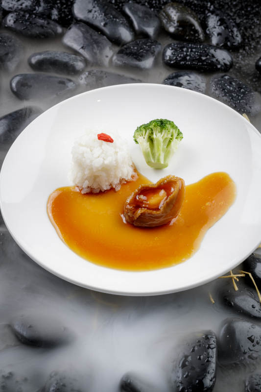 鲍汁捞饭摆放在干冰缭绕的黑色鹅卵石上