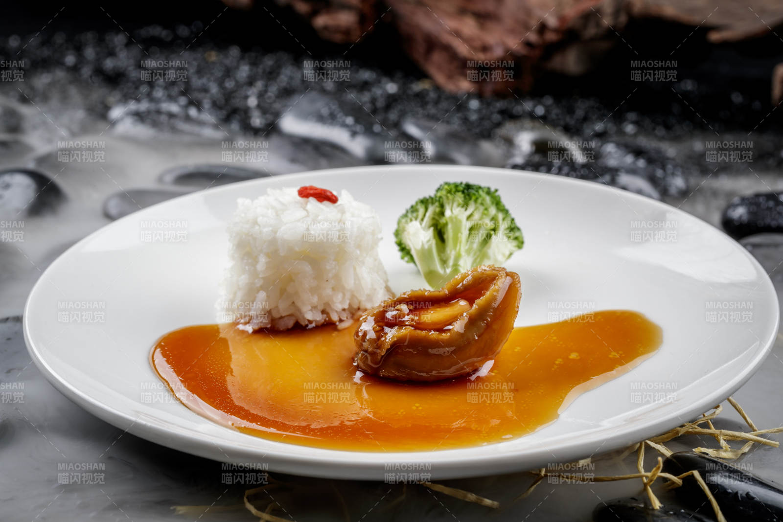 鲍汁捞饭摆放在干冰缭绕的黑色鹅卵石上