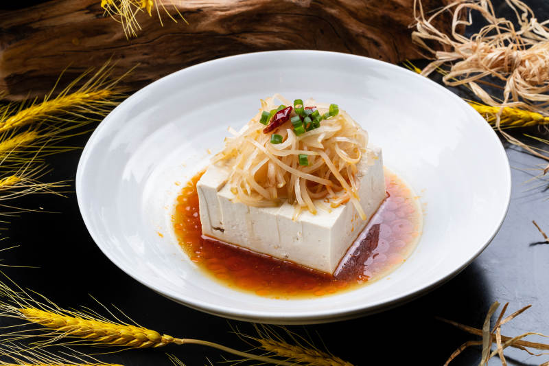 圆形瓷盘装的一品豆腐摆放在黑色背景上