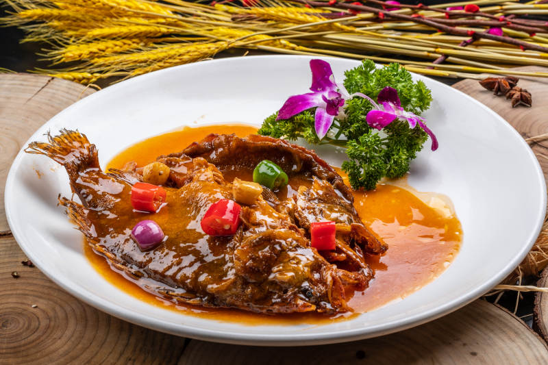 白色圆盘装的红烧罗非鱼摆放在樟木砧板上