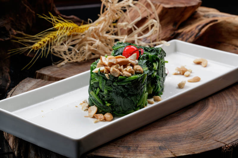 長方形瓷盤裝的菠菜卷擺放在樟木砧板上