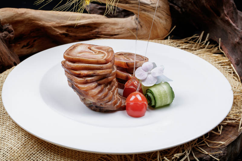 白色圆盘装的烟熏猪耳卷摆放在麻布垫子上