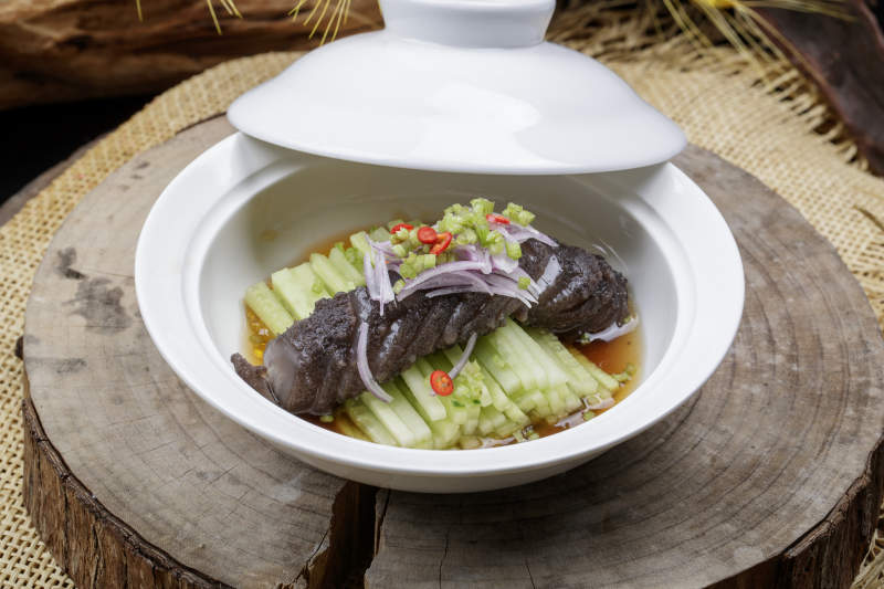 白色汤碗装的锅烧大海参摆放在樟木砧板上