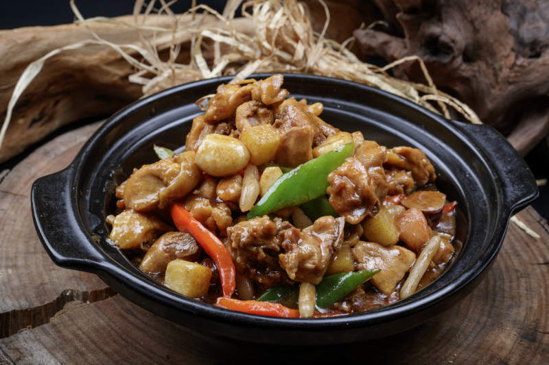 黑色砂锅装的砂锅蒜香鸡摆放在樟木砧板上