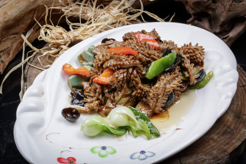 橢圓瓷盤裝的臘八蒜炒腰花擺放在樟木砧板上