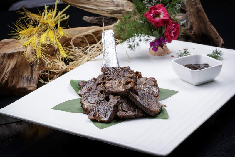 方形瓷盘装的炭烤牛肋排摆放在黑色背景上