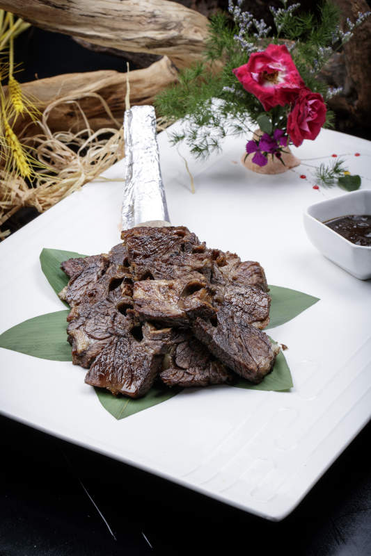 方形瓷盘装的炭烤牛肋排摆放在黑色背景上