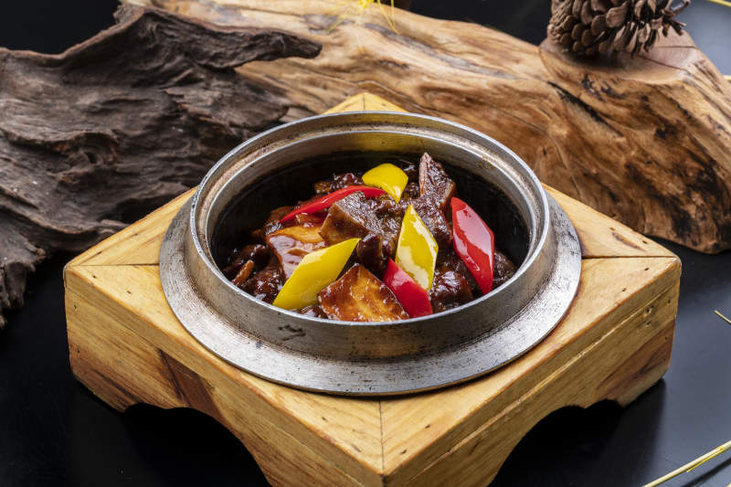 木托鐵鍋裝的醬爆牛仔骨擺放在黑色背景上