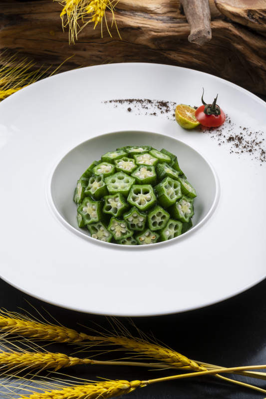 圓形瓷盤裝的撈汁鮮秋葵擺放在黑色背景上