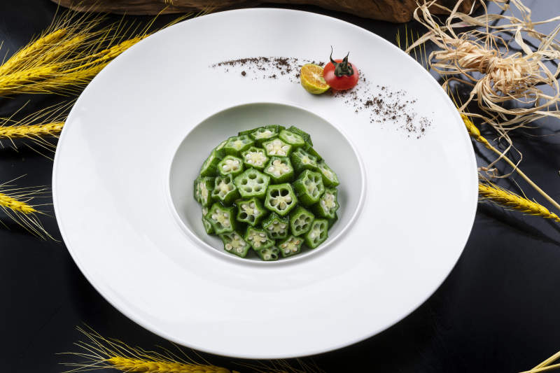 圓形瓷盤裝的撈汁鮮秋葵擺放在黑色背景上