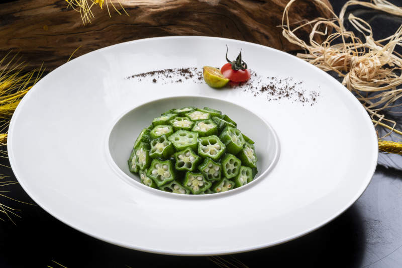 圓形瓷盤裝的撈汁鮮秋葵擺放在黑色背景上