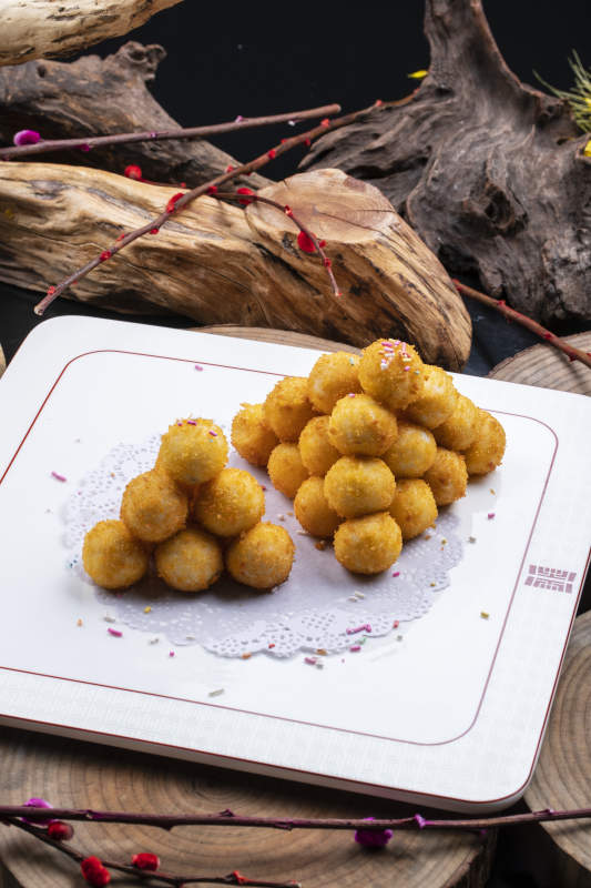 方形瓷盘装的黄金炸汤圆摆放在樟木砧板上