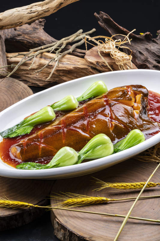 椭圆瓷盘装的红烧鲽鱼尾摆放在樟木砧板上