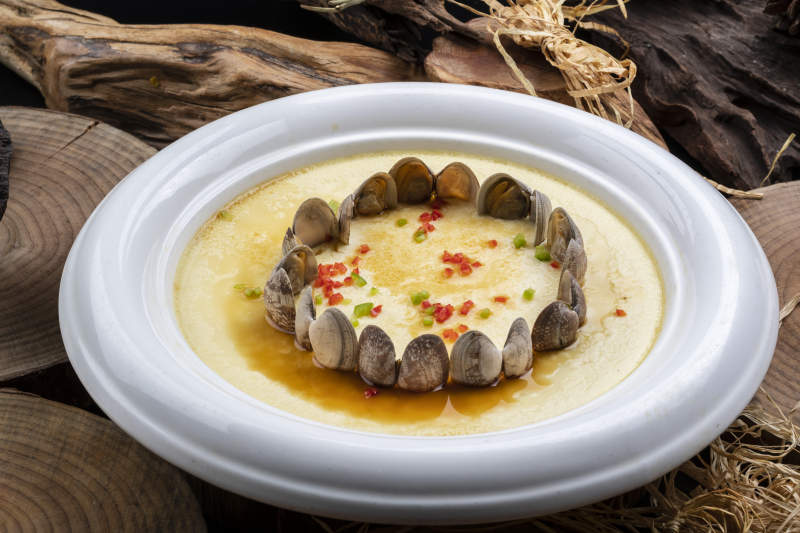 白色圆盘装的花蛤蒸蛋摆放在樟木砧板上