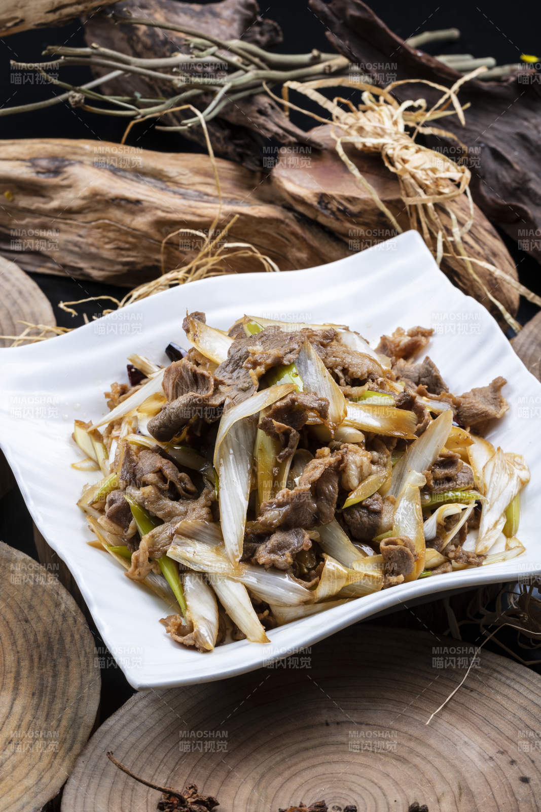 方形花瓷盘装的大葱爆羊肉摆放在樟木砧板上