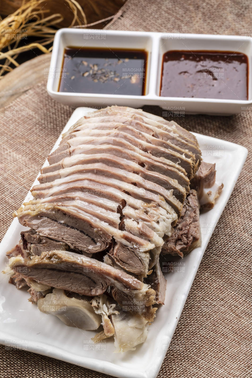 長方形瓷盤裝的白灼羊背擺放在麻布墊子上