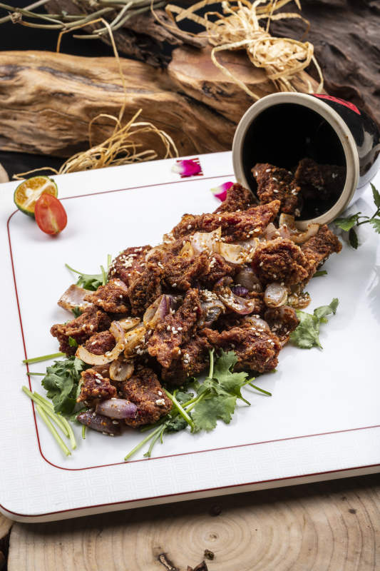 方形瓷盤裝的孜然羊肉擺放在樟木砧板上