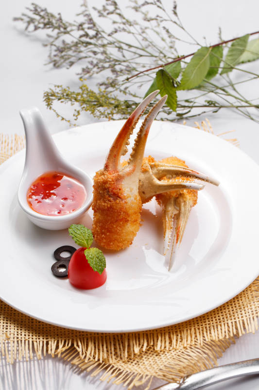 白色圆盘装面包糠芝士焗梭蟹钳摆放在草垫上