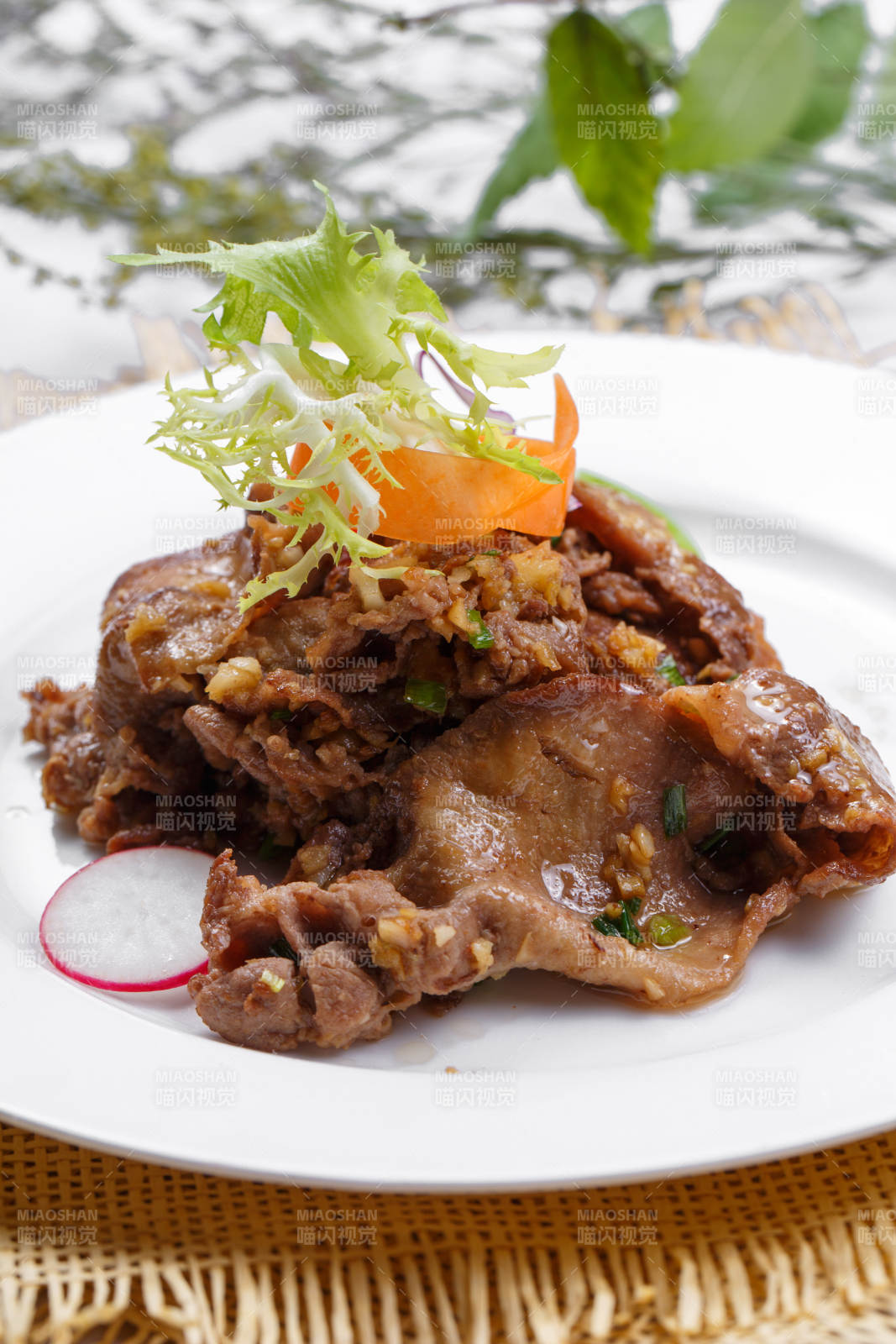 圆形白瓷盘装的铁板蒜香牛舌摆放在草垫上