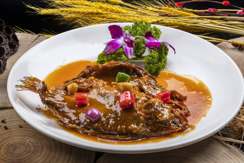 白色圆盘装的红烧罗非鱼摆放在樟木砧板上