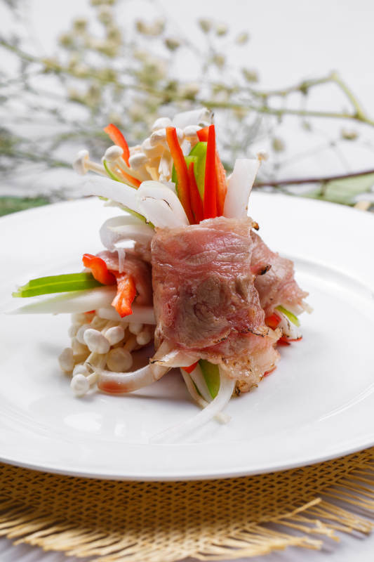 白色圆盘装的法式鹅肝牛肉卷摆放在草垫上