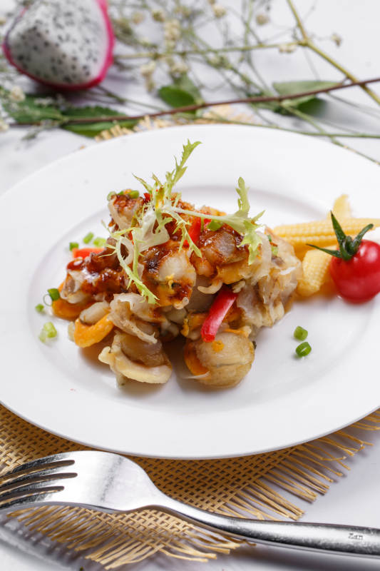 白色瓷盘装的铁板香辣扇贝肉摆放在草垫上