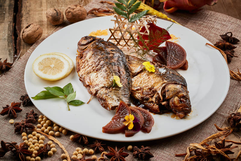 陈旧木板上的圆瓷盘装的家炖香酥鲫鱼