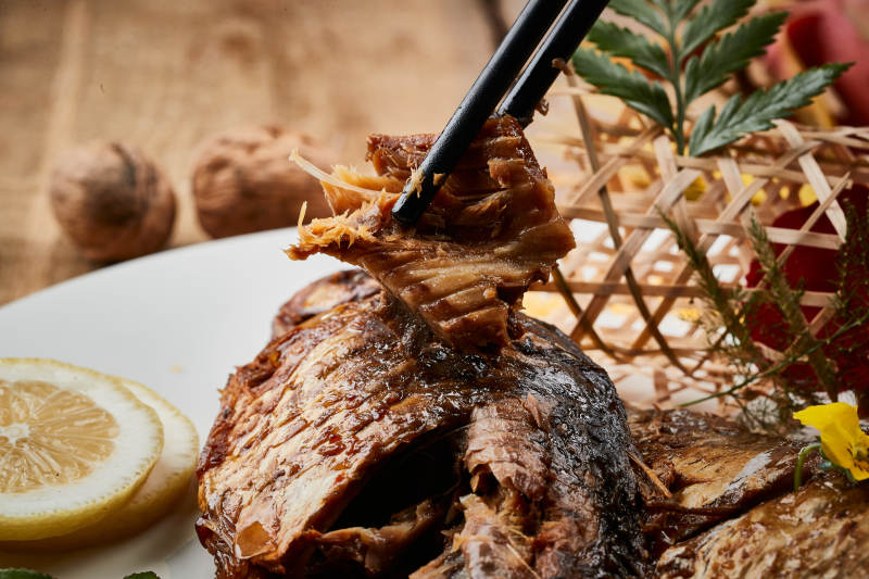 陈旧木板上的圆瓷盘装的家炖香酥鲫鱼