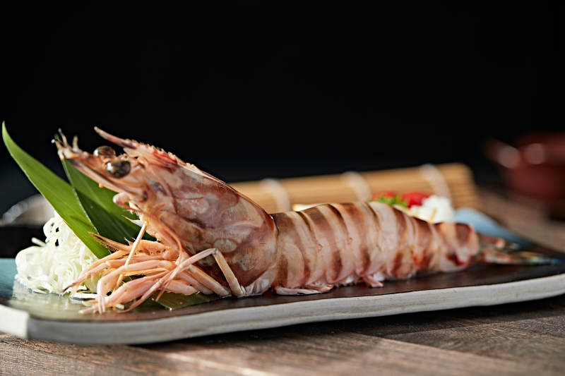 长方形瓷盘装的铁板野生明虾皇摆放在草垫上