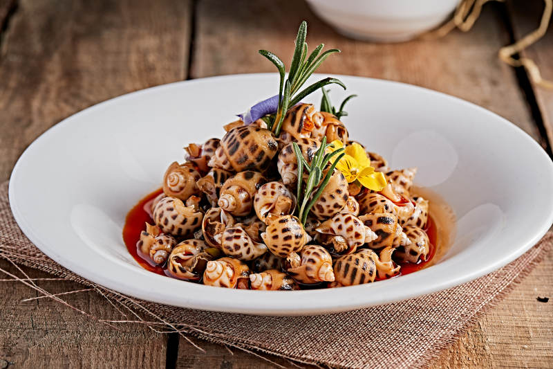 白色瓷盘装的红油腌渍小花螺