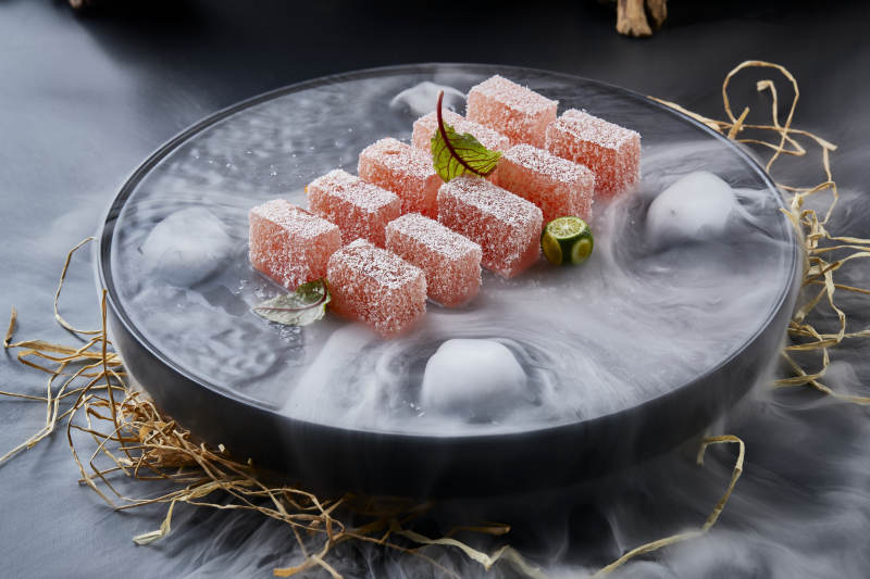 干冰缭绕的黑瓷餐具摆放的番茄糖霜江米糕