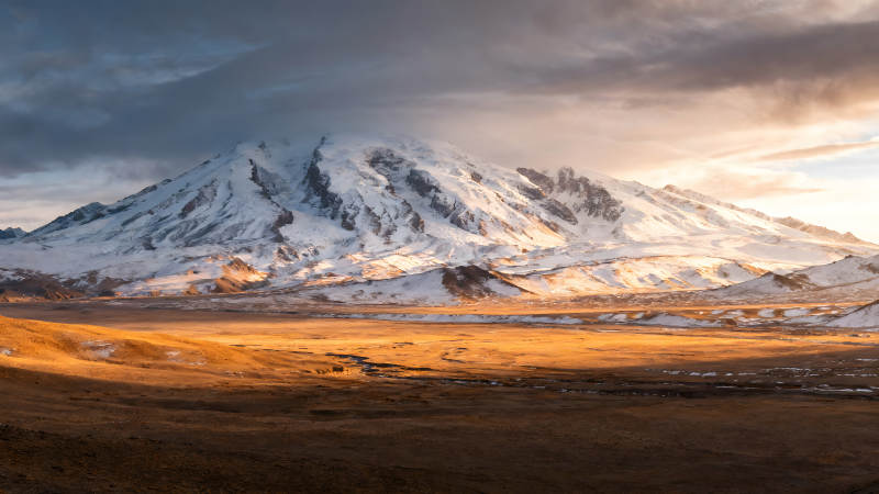 雪山下的金色平原陽光照射下的壯麗景色-圖片
