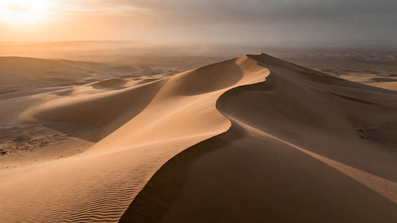 沙漠沙丘在陽光下形成曲線-圖片