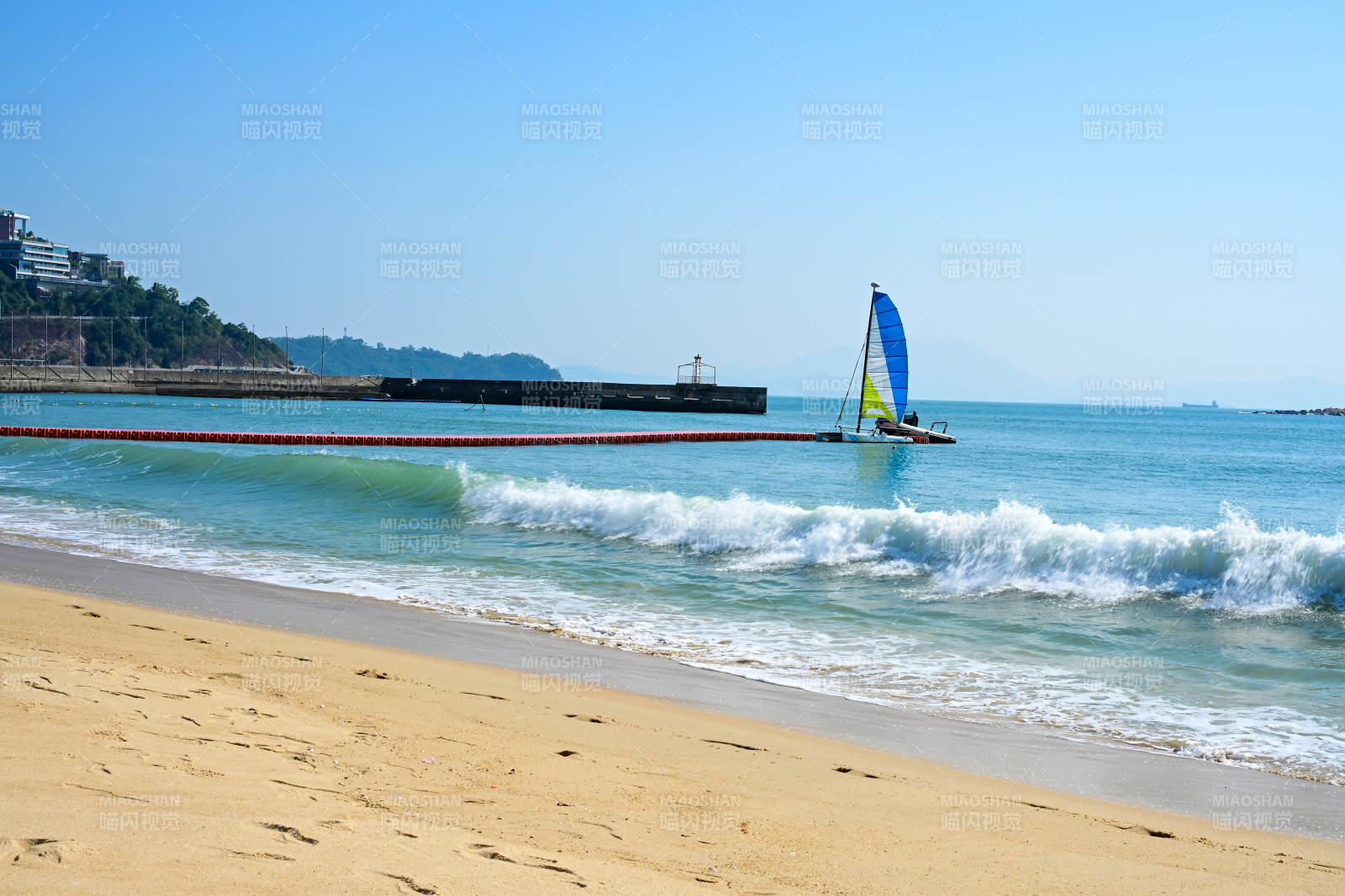 深圳大梅沙海滩边的蓝色帆船与海浪景观图片