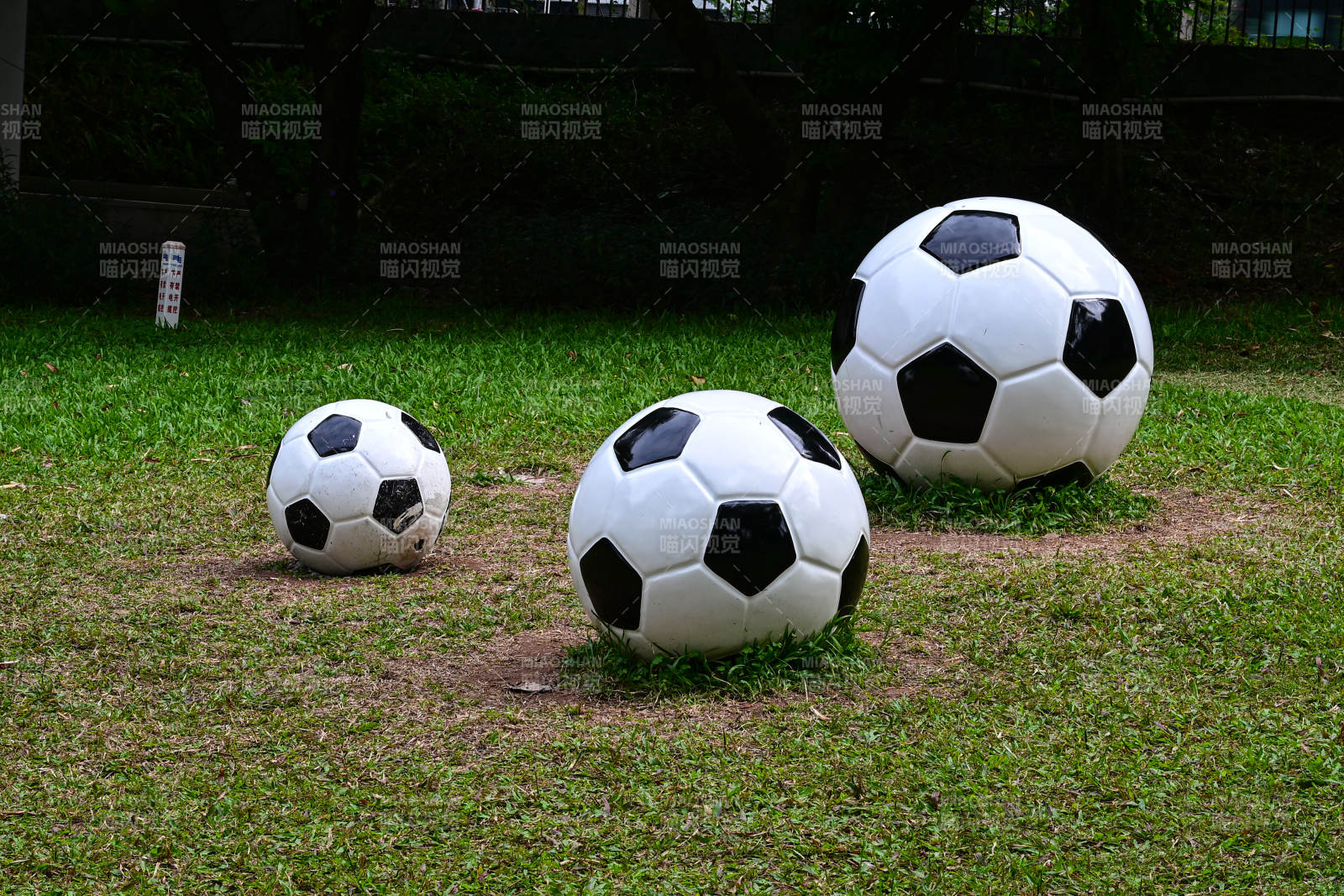 户外草坪上大小不一的三个足球雕塑艺术图片