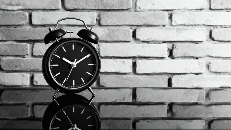 复古闹钟静置砖墙前图片